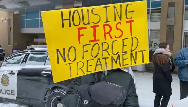 A sign held outside the Hyatt Regency in Calgary reads "Housing First No Forced Treatment." 